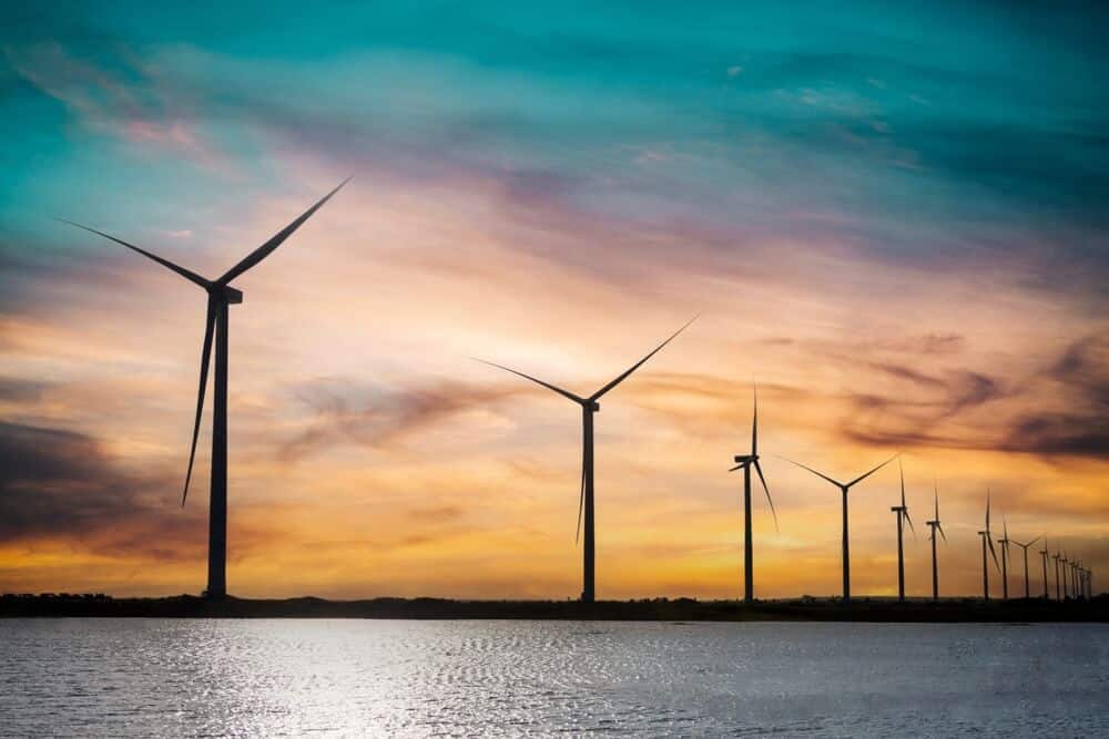 Clean energy windmills on the ocean with a sunset in the background.