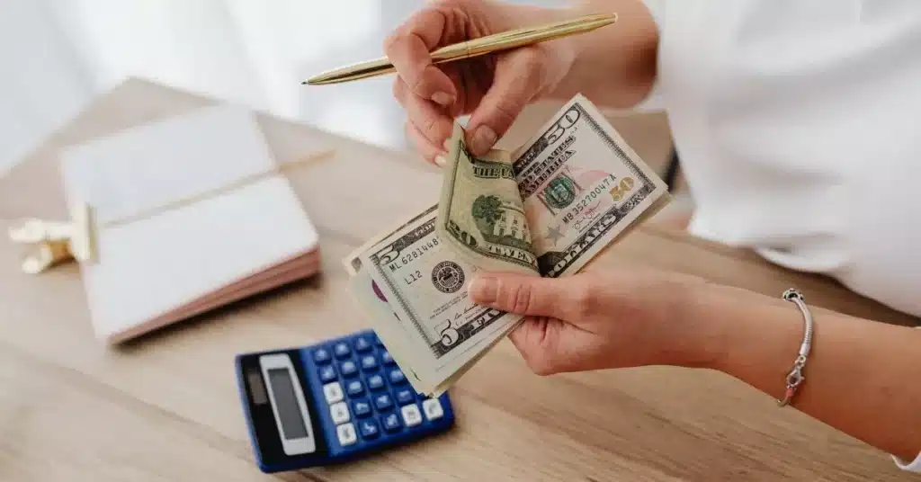 Product funding planning shown by a founder counting cash next to a calculator and notebook.